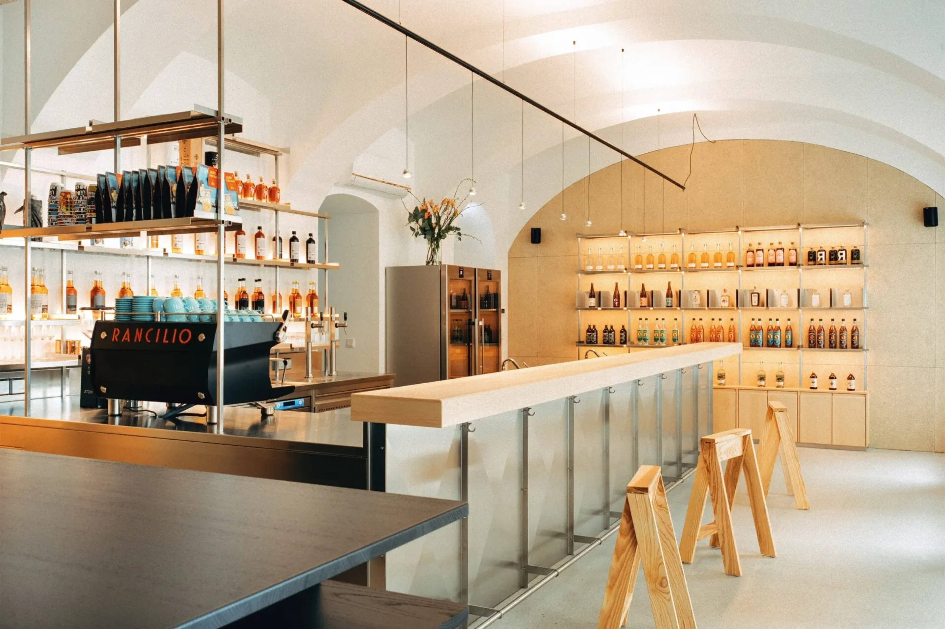 Blick über Bar und Espressomaschine zum beleuchteten Flaschenregal unter dem Gewölbe